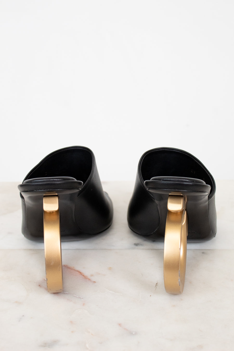 Pair of black shoes with gold heel on a marble surface