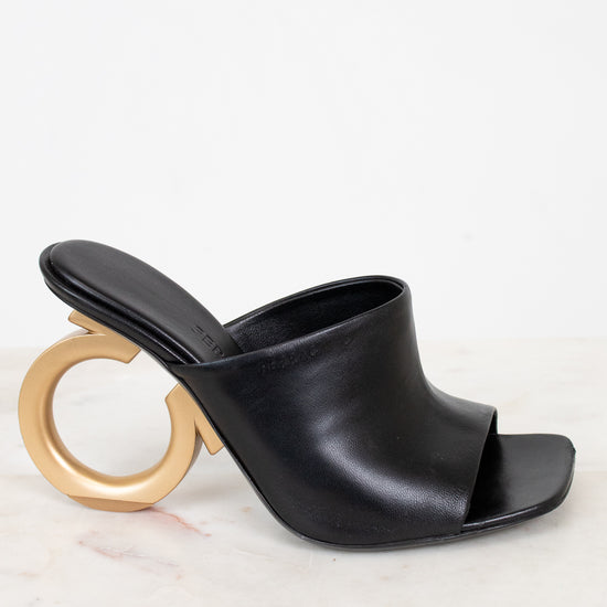 Black open-toe sandal with a gold ring heel on a white background