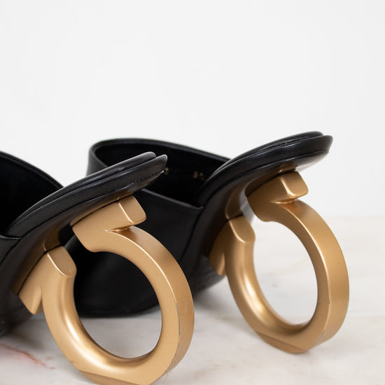 Black heeled shoe with golden heel detail on a light background