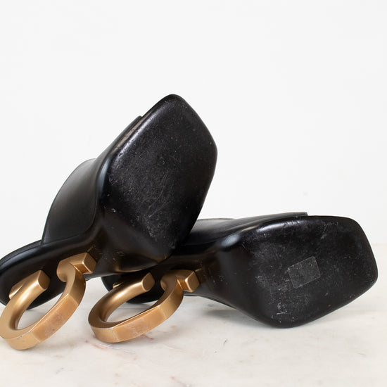 Black high-heeled shoes with gold heel detail on a white background