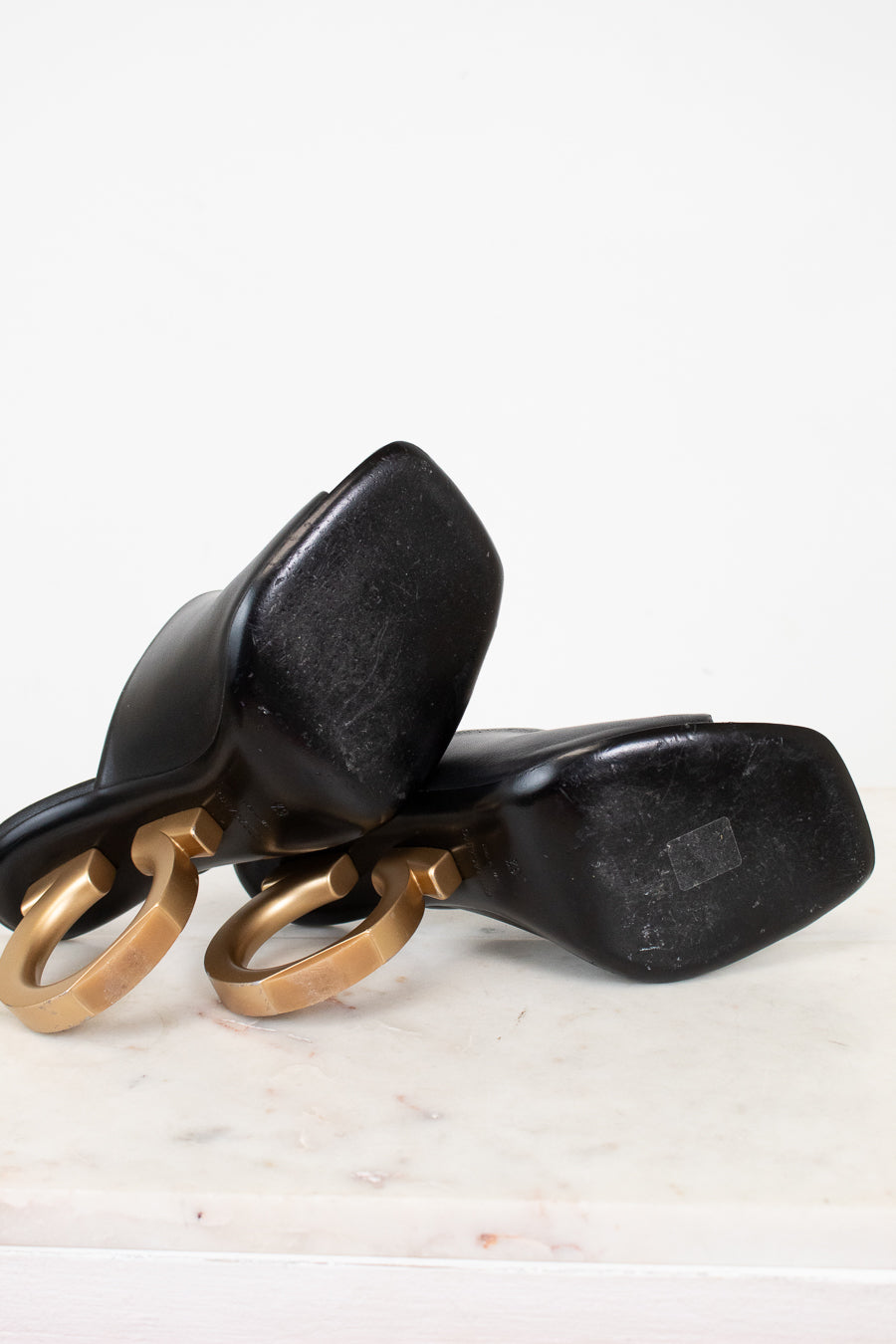 Black high-heeled shoes with gold heel detail on a white background