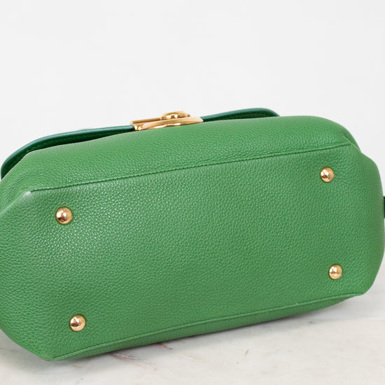 Bottom view of green handbag with gold feet on a white marble surface