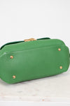 Bottom view of green handbag with gold feet on a white marble surface