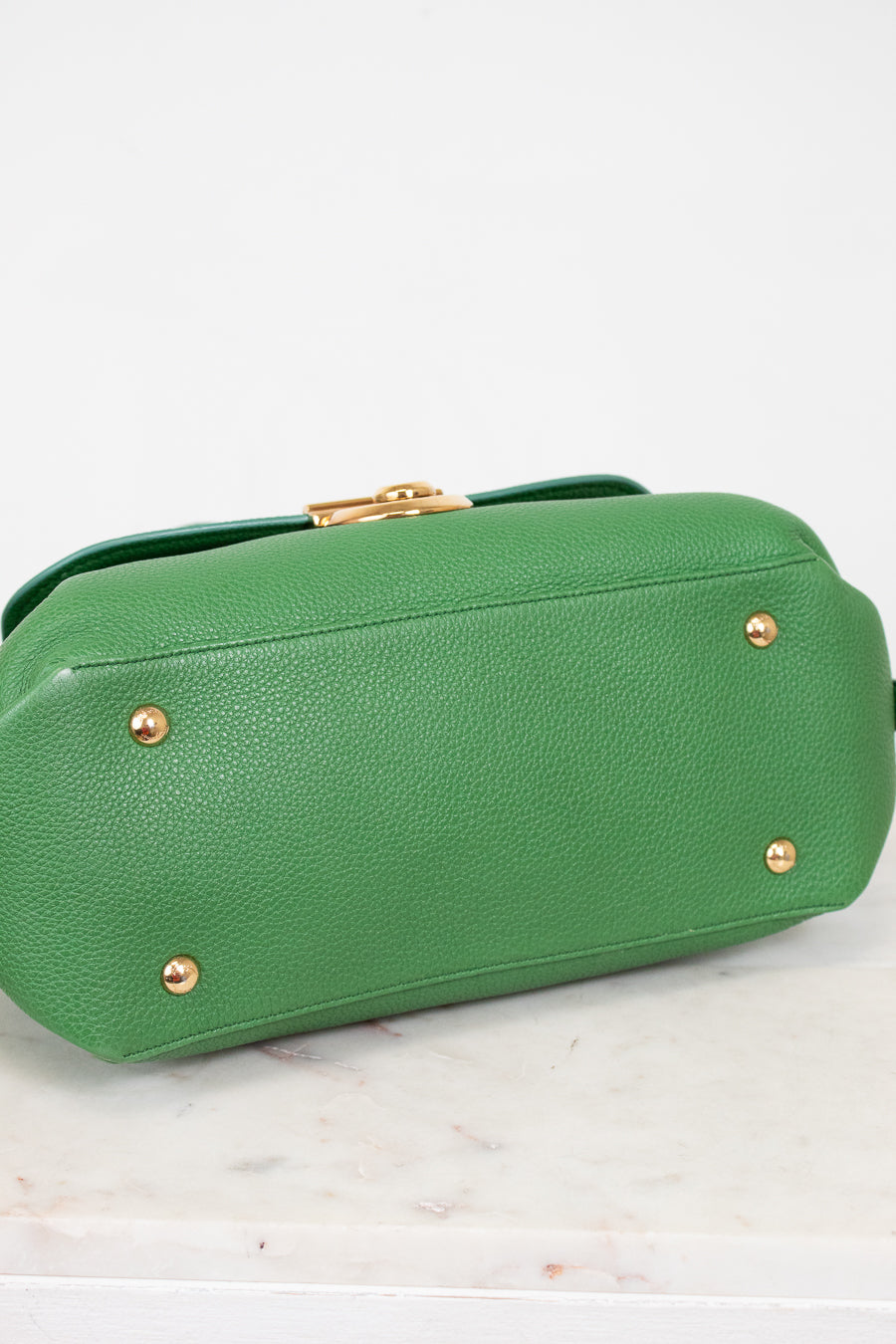 Bottom view of green handbag with gold feet on a white marble surface