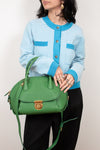Person wearing a light blue cardigan with green accents, holding a green handbag against a plain background