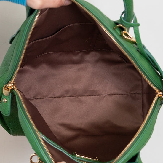 Green handbag with gold accents held open by a hand against a neutral background
