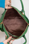 Green handbag with gold accents held open by a hand against a neutral background