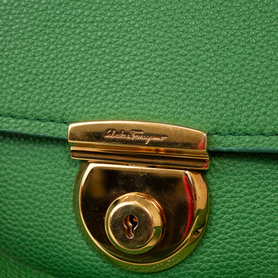 Close-up of a green handbag with a gold lock and 'Salvatore Ferragamo' branding.