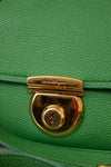 Close-up of a green handbag with a gold lock and 'Salvatore Ferragamo' branding.