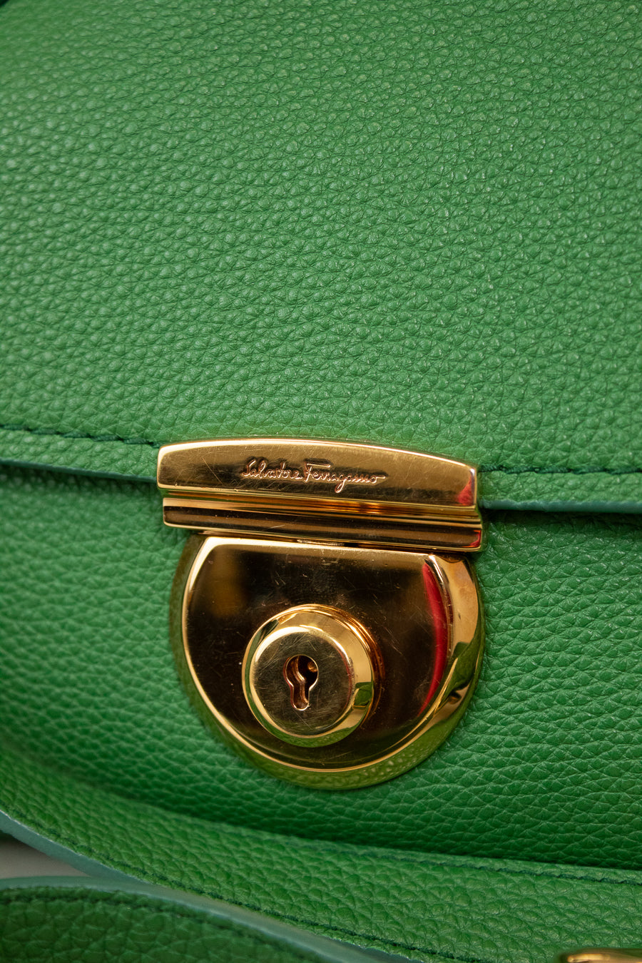 Close-up of a green handbag with a gold lock and 'Salvatore Ferragamo' branding.