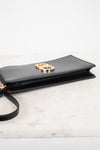 A black leather clutch bag with a gold-tone interlocking logo on the front, resting on a white marble surface against a white background.