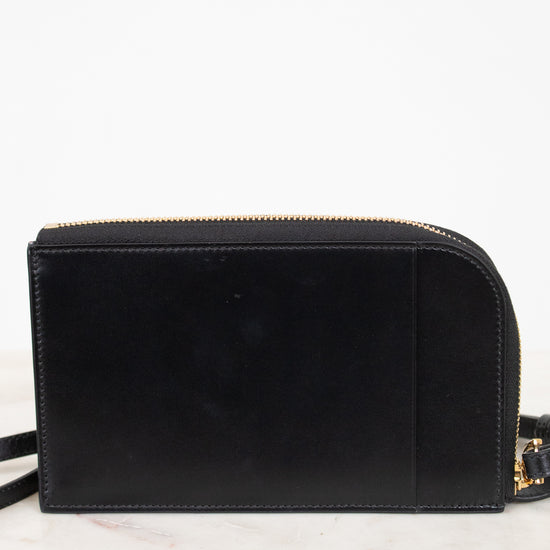 A black leather crossbody bag with gold-tone hardware, resting on a white marble surface against a white background.