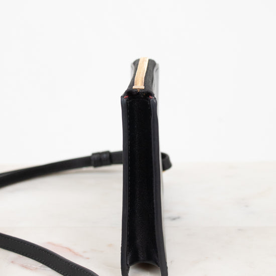 A black leather crossbody bag shown from a side profile view, featuring a gold zipper accent and a thin black strap, set against a clean white background.