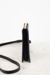 A black leather crossbody bag shown from a side profile view, featuring a gold zipper accent and a thin black strap, set against a clean white background.