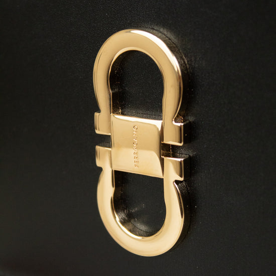 Close-up of a black leather handbag featuring a large polished gold-tone  buckle hardware on the front.
