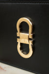 Close-up of a black leather handbag featuring a large polished gold-tone  buckle hardware on the front.