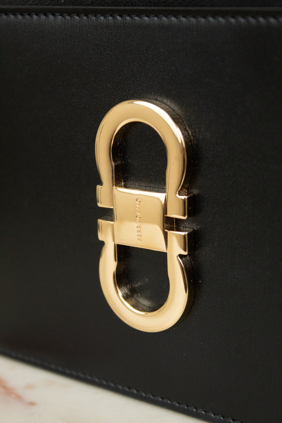 Close-up of a black leather handbag featuring a large polished gold-tone  buckle hardware on the front.