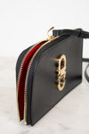 A black leather clutch bag with a gold-tone metal zipper and a vibrant red interior lining, shown on a light marble surface against a white background.