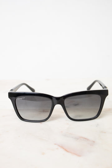 Black cat-eye sunglasses with gradient gray lenses, displayed on a light marble surface against a white background.