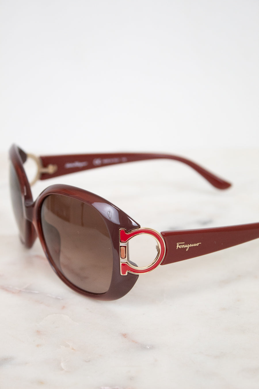 Salvatore Ferragamo sunglasses with brown lenses and red frame on a light background