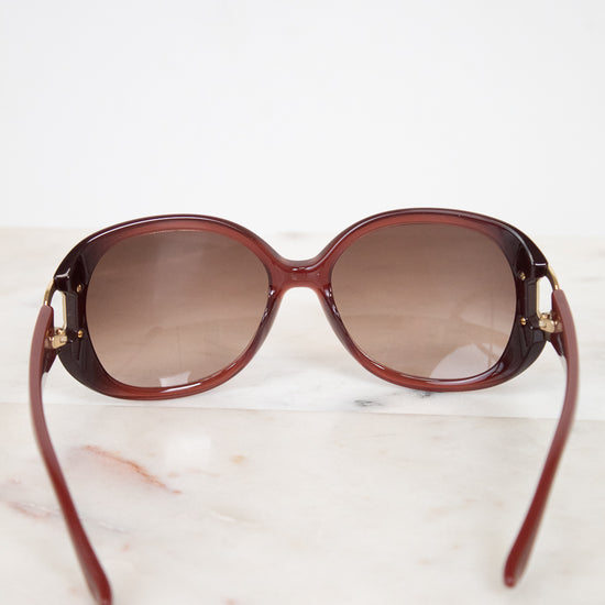 Maroon sunglasses with gradient lenses on a light marble background