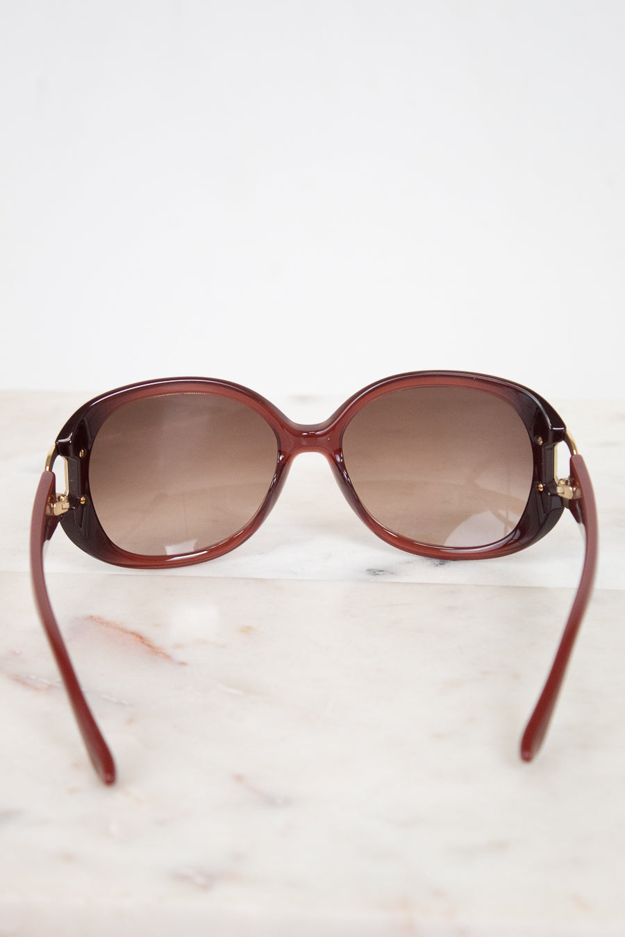 Maroon sunglasses with gradient lenses on a light marble background