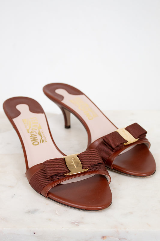 Brown high-heeled shoes with gold accents on a light background