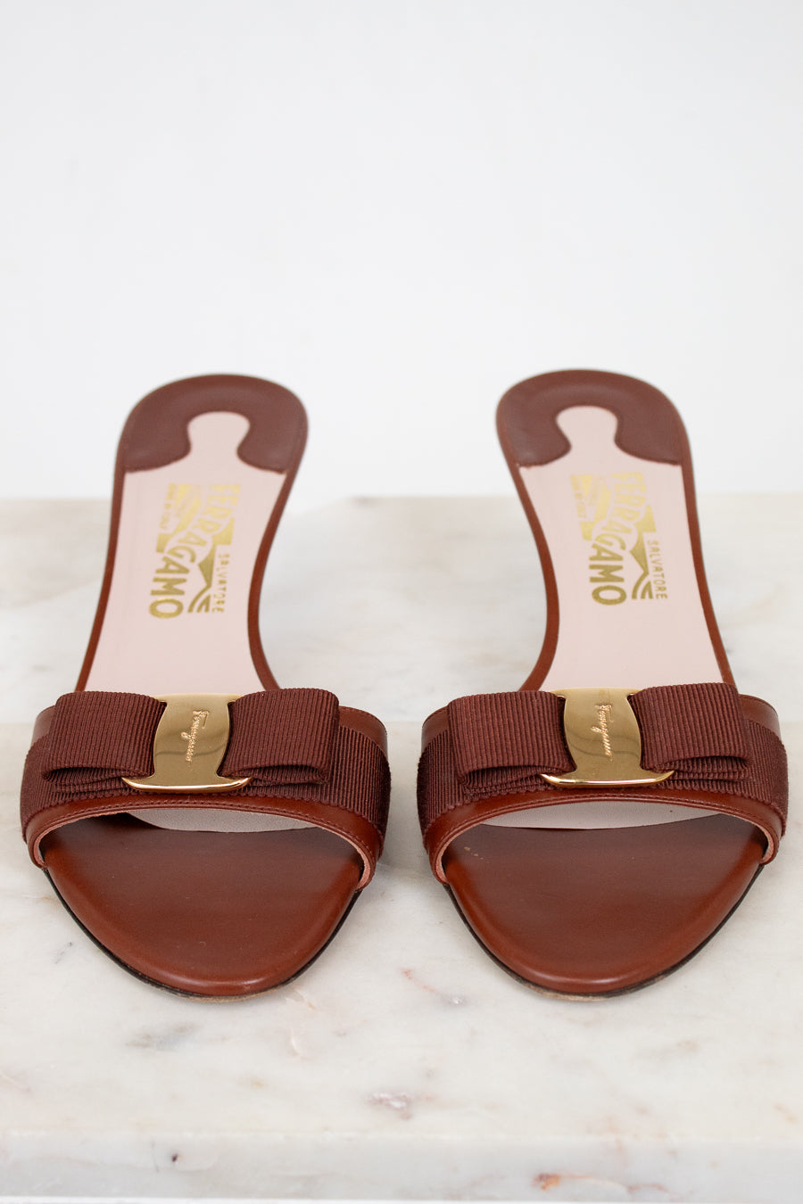 Pair of brown sandals with gold accents on a white marble surface