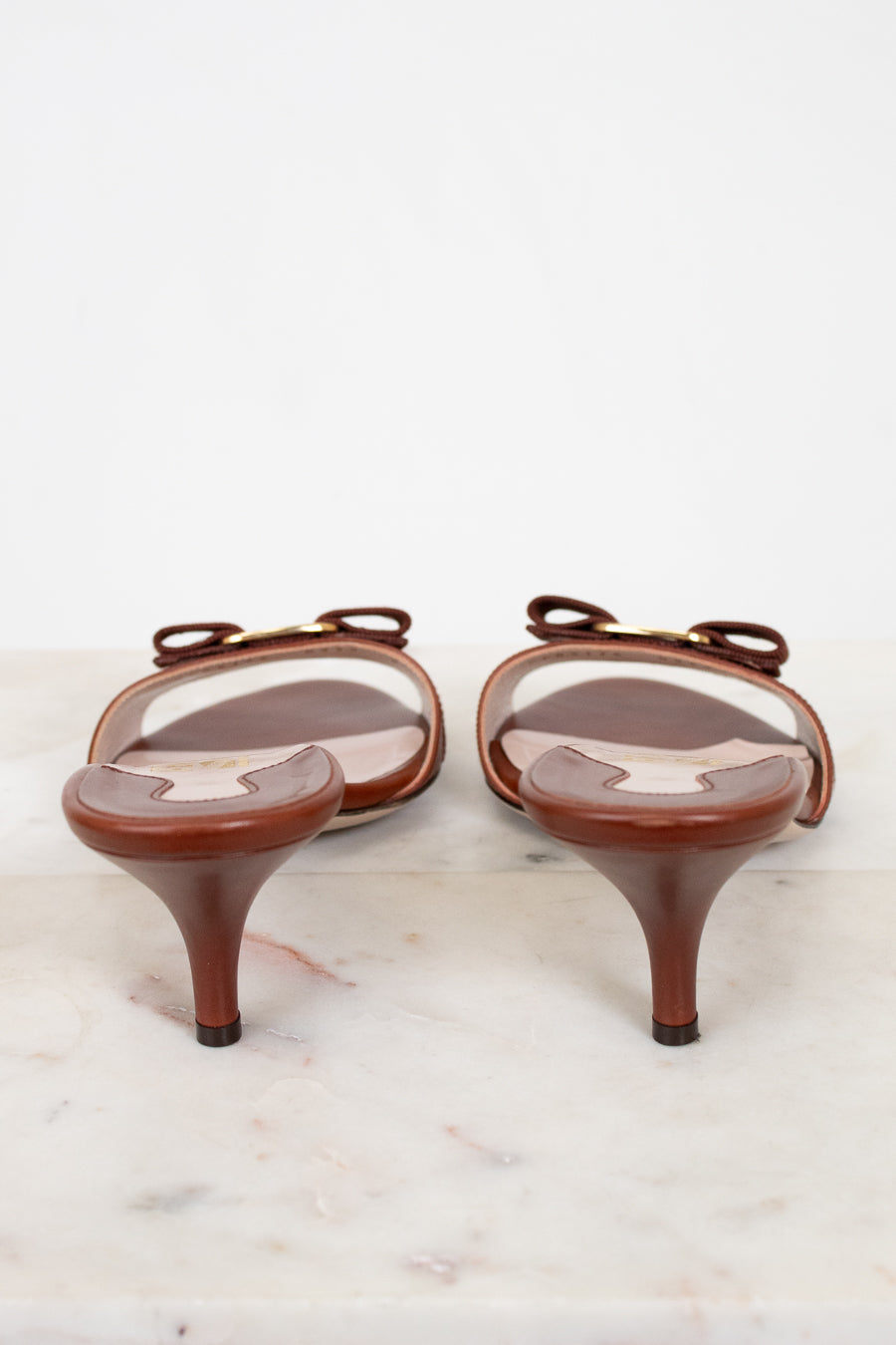 Pair of brown high-heeled shoes with clear covers on a white marble surface