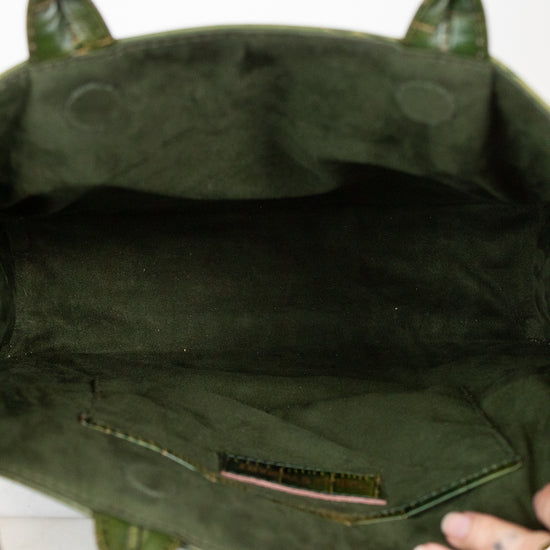 Close-up of the interior of an olive green suede handbag, showing the lining, a small interior pocket, and a hand holding the bottom edge.
