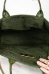 Close-up of the interior of an olive green suede handbag, showing the lining, a small interior pocket, and a hand holding the bottom edge.