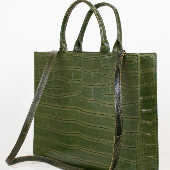 An olive green crocodile-embossed leather tote bag with dual top handles and a detachable shoulder strap, displayed on a light marble surface against a white background.