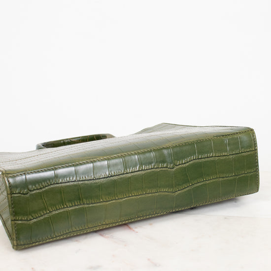 An olive green crocodile-embossed leather clutch bag resting on a white marble surface against a white background.