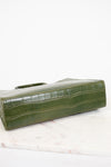 An olive green crocodile-embossed leather clutch bag resting on a white marble surface against a white background.