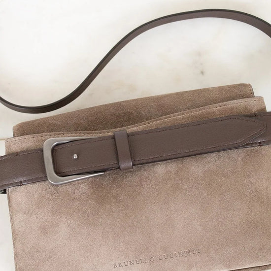 Beige suede handbag with a brown leather strap on a light background