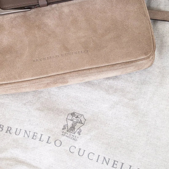 Brown suede handbag with leather strap on a textured surface, featuring Brunello Cucinelli branding.