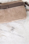 Brown suede handbag with leather strap on a textured surface, featuring Brunello Cucinelli branding.