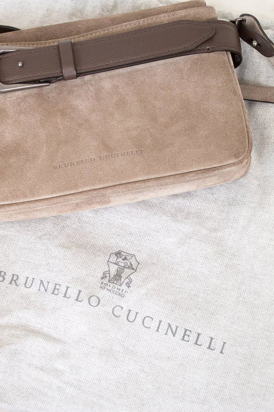 Brown suede handbag with leather strap on a textured surface, featuring Brunello Cucinelli branding.
