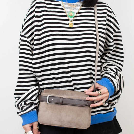 Person wearing a black and white striped sweater with blue accents, holding a beige handbag.