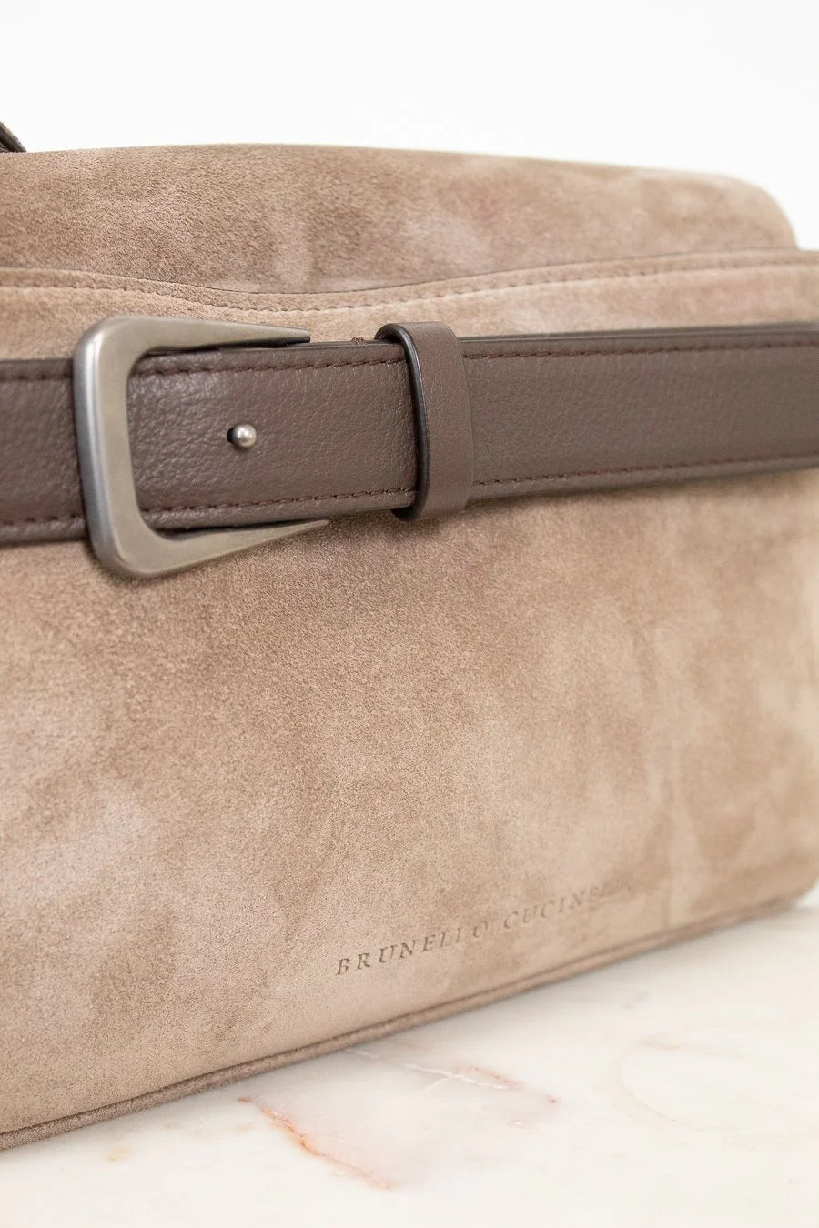 Beige handbag with a brown leather strap on a marble surface