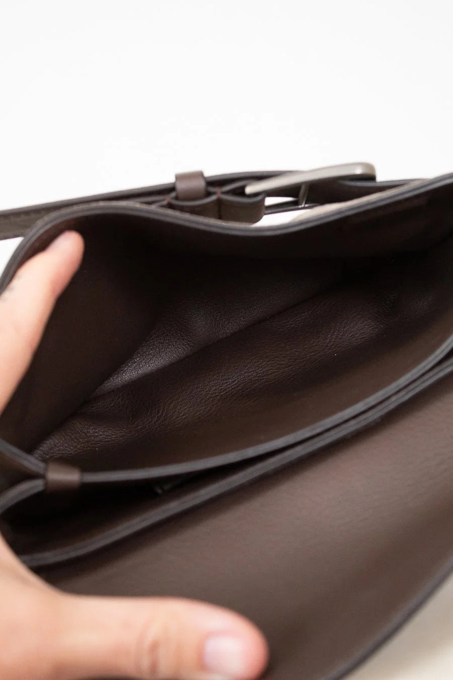 Close-up of a interior brown leather on suede bag with a hand opening it on a white background