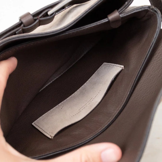 Brown leather interior of bag with a visible brand label held by a hand on a light background
