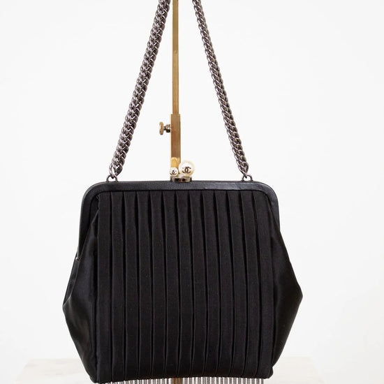 Black handbag with chain strap and fringe details on a white background