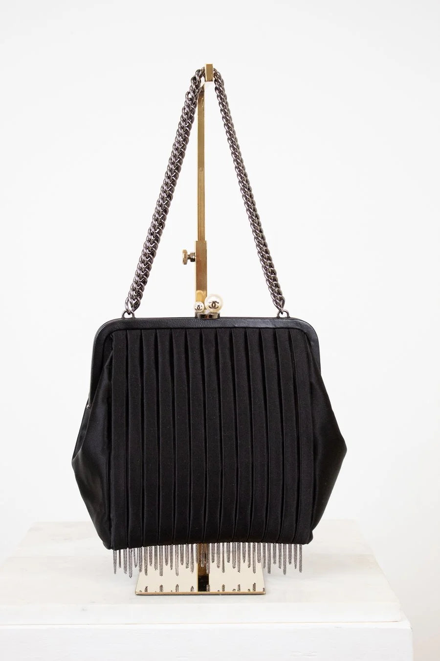 Black handbag with chain strap and fringe details on a white background