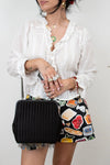 Person wearing a white blouse and colorful shorts with a black handbag.