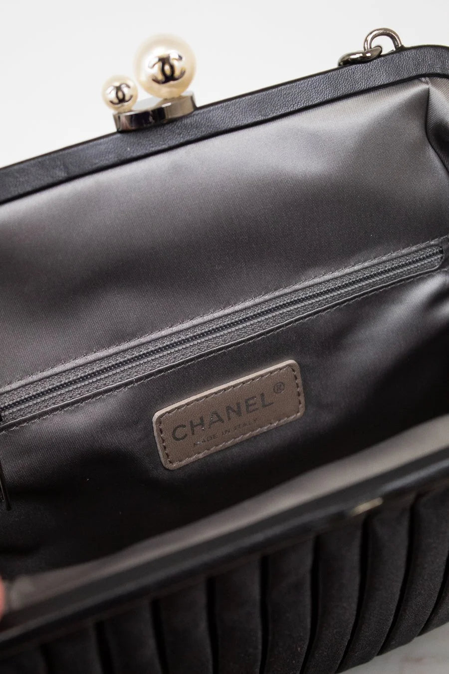 Close-up of a Chanel handbag with a silver/pearl clasp on a light gray background