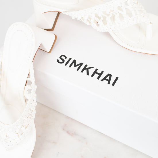 White block heeled sandals with white box branded 'SIMKHAI' on a marble surface