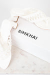 White block heeled sandals with white box branded 'SIMKHAI' on a marble surface