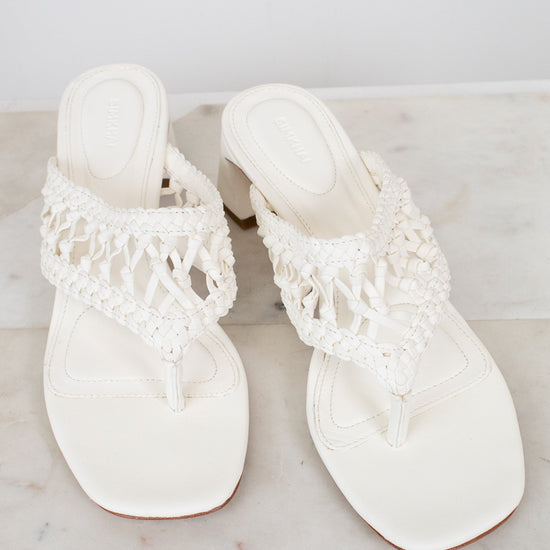 Pair of white sandals with crochet straps on a marble surface