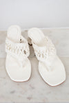 Pair of white sandals with crochet straps on a marble surface